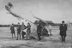 Flygplan Albatros SW 20 nummer 750 har landat på nosen på Flygkompaniet på Malmen, vintertid 1919. Folksamling vid flygplanet. Från vänster verkmästare Jonasson, löjtnant Tor Klintberg, furir Seigertz, flygförare Mats E. Berg, verkmästare Theodor Pettersson. I bakgrunden syns Röda förrådet.