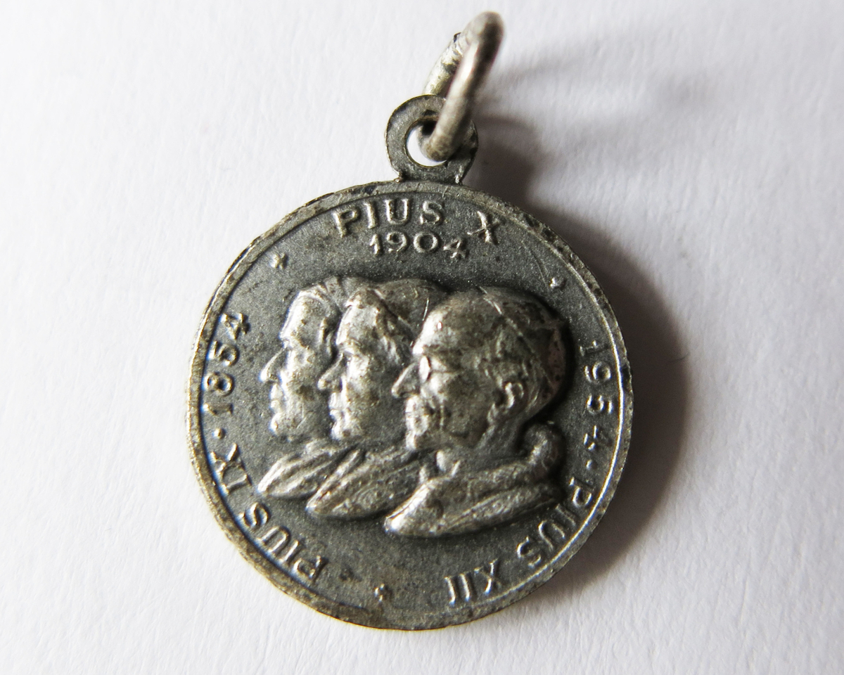 Motiv advers: Pavene Pius IX, Pius X og Pius XII, byster i profil mot venstre.

Motiv revers: Jomfru Maria i Lourdes med knelende Bernadette, nederst den mirakuløse medaljens advers og revers.