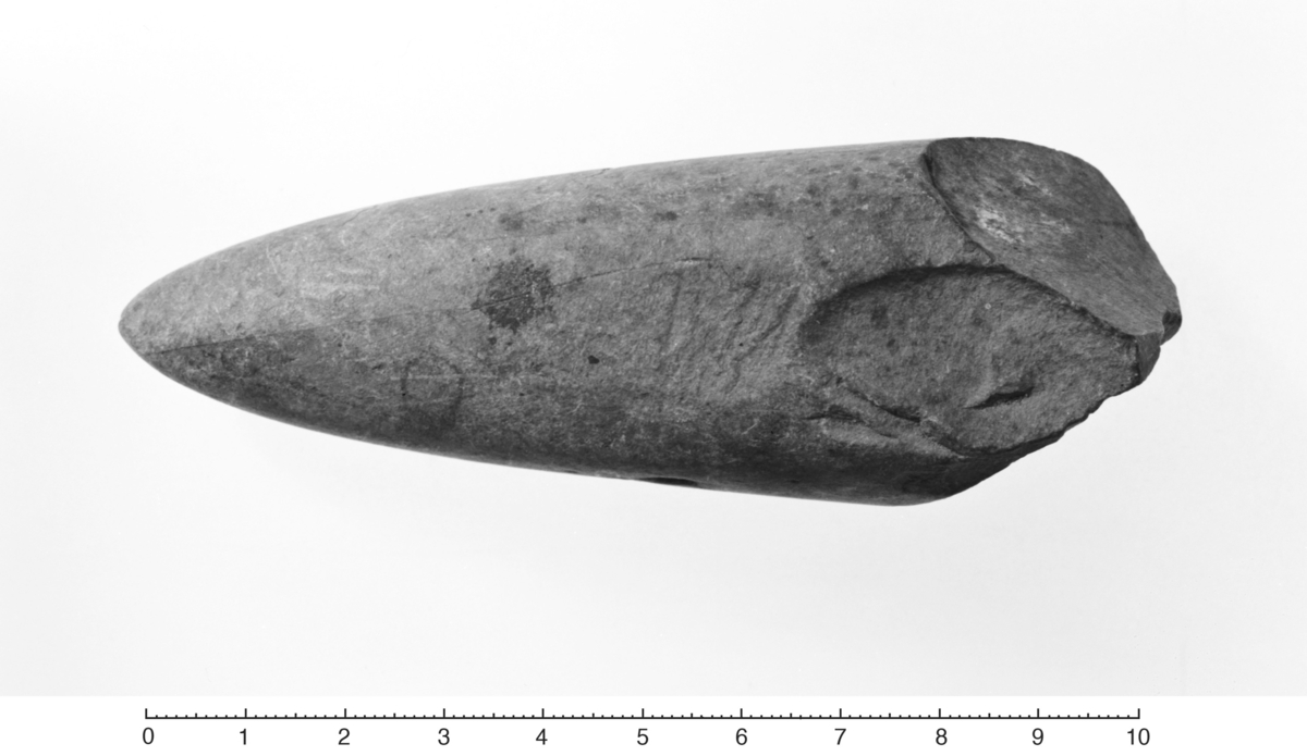 "Nakkestykke av spissnakket trindøks, Gjessing: Rogalands Stenalder, fig. 61 etc. , udmerket fasettslipt over det hele. Lengden er nu 10,7 cm. I bruddstedet er øksen nu skråhugget til to sider, som om man vilde anlegge ny egg." Tilleggsopplysning: Grønnsteinen er fra Hespriholmen, Alsaker 1987: Bømlo -Steinalderens råstoffsentrum på Sørvestlandet, s. 58.