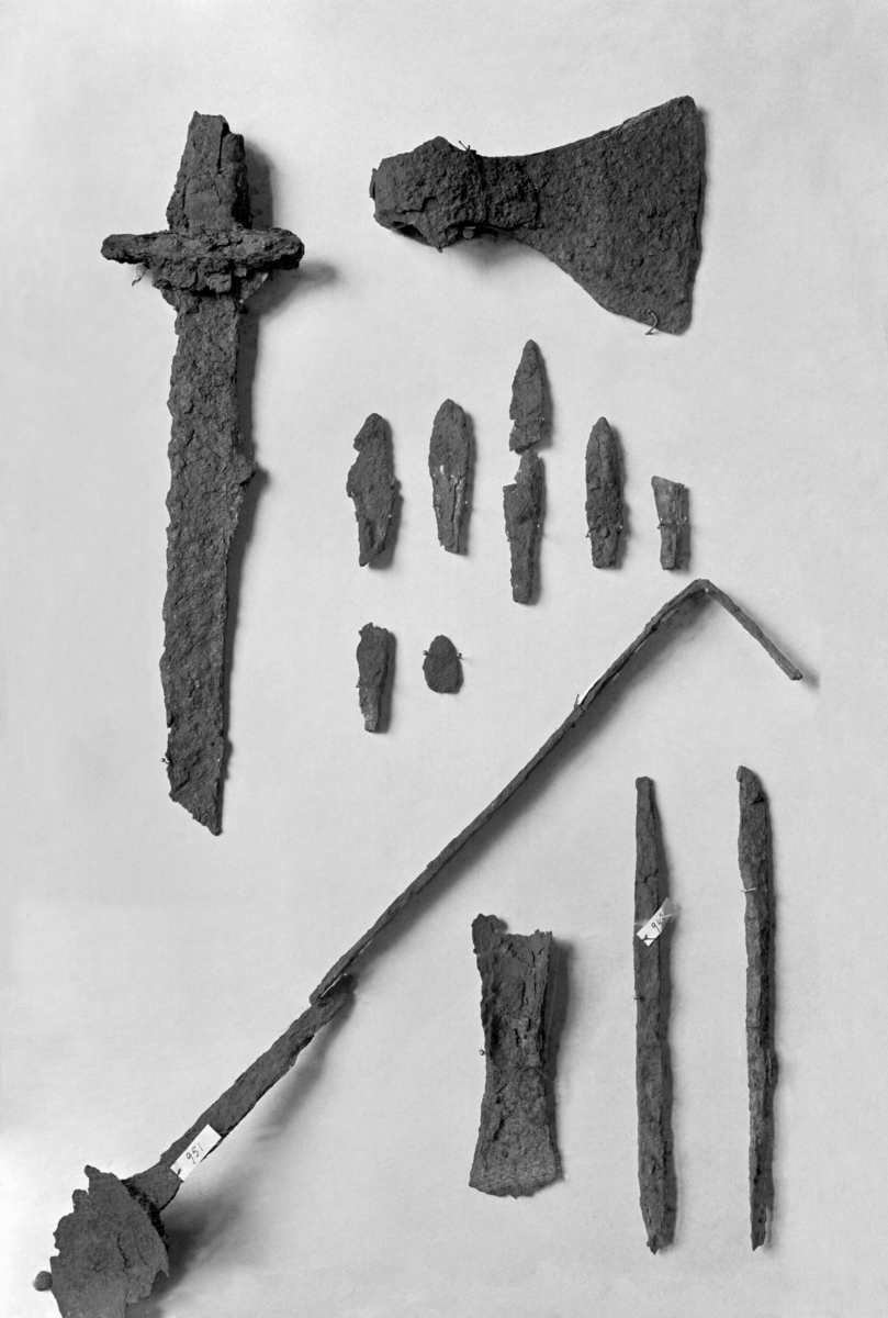 Hovedkatalogen: "Sværd af Jern, Fragment, Grebtangen der er bevaret er over 4 Tom. [10,4 cm] lang; noget af Parerpladen er igjen, forresten yderst medtaget af Rust."
Revisjon 2019: Eit 16,5 cm langt fragment av ein sverdklinge, med defekte eggar. Fått undernr a ved revisjon. Unummererte naglar frå same funn registrert som unr b. 
Sverdet er et Ulfberth-sverd. Det er utydelige rester av navnet, der BERH+T er synlig. 

