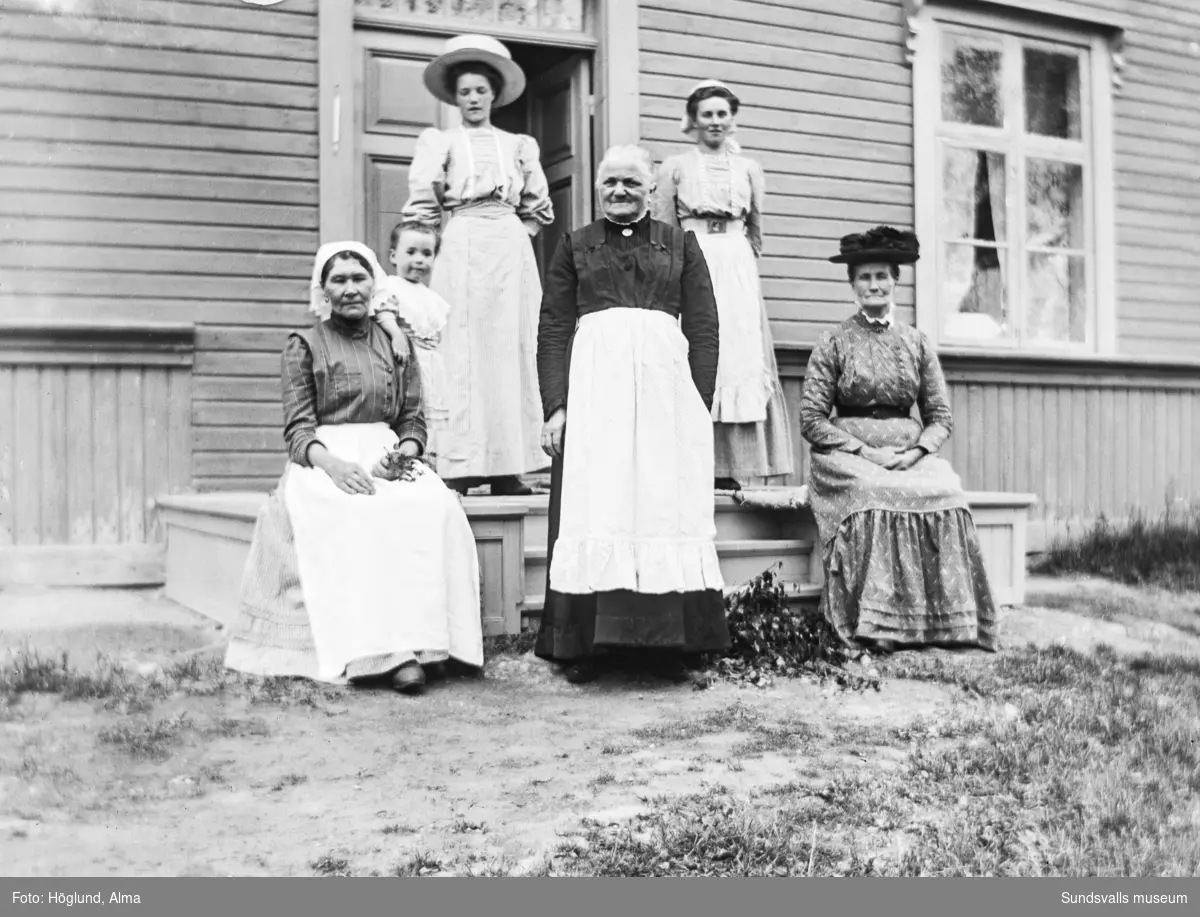Gruppbild framför Höglund bostad på Hammarn i Fanbyn. Barnet är Hilma Höglund och bakom står hennes moster Jenny Wiström. Övriga fyra kvinnor är oidentifierade.