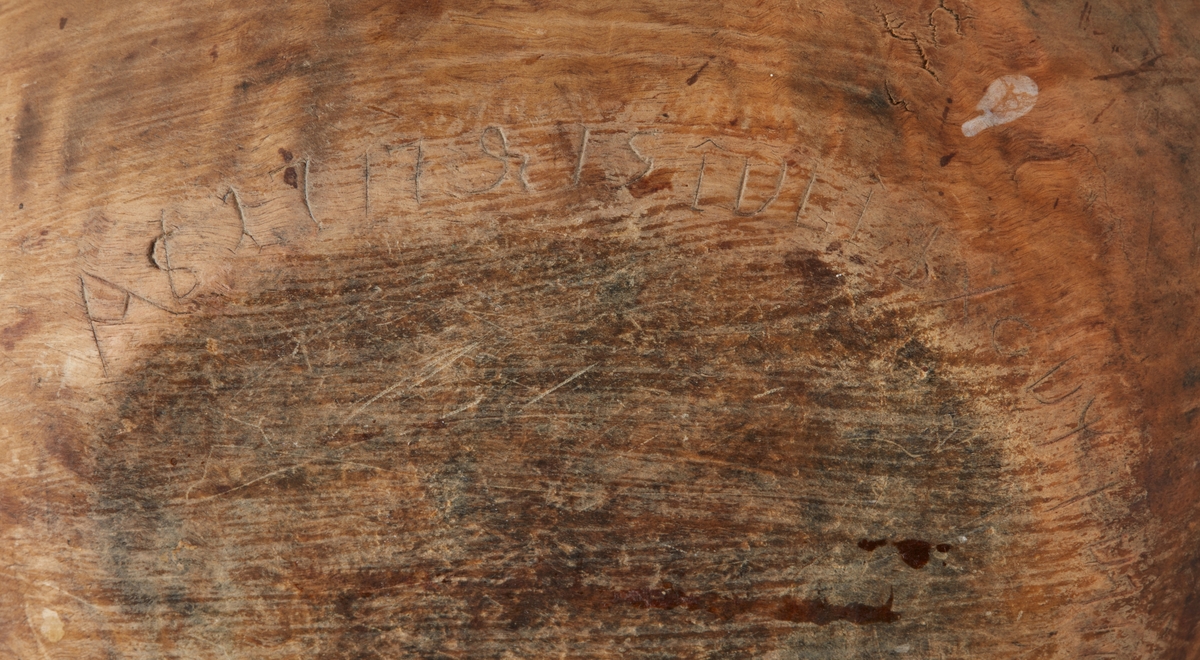 Skål av trä. En stor spricka i ena kortsidan lagad med mässingstråd. Runt botten inristade dalrunor, bla årtal: "1717".
Bilagor finns med en del tolkningar av runorna.