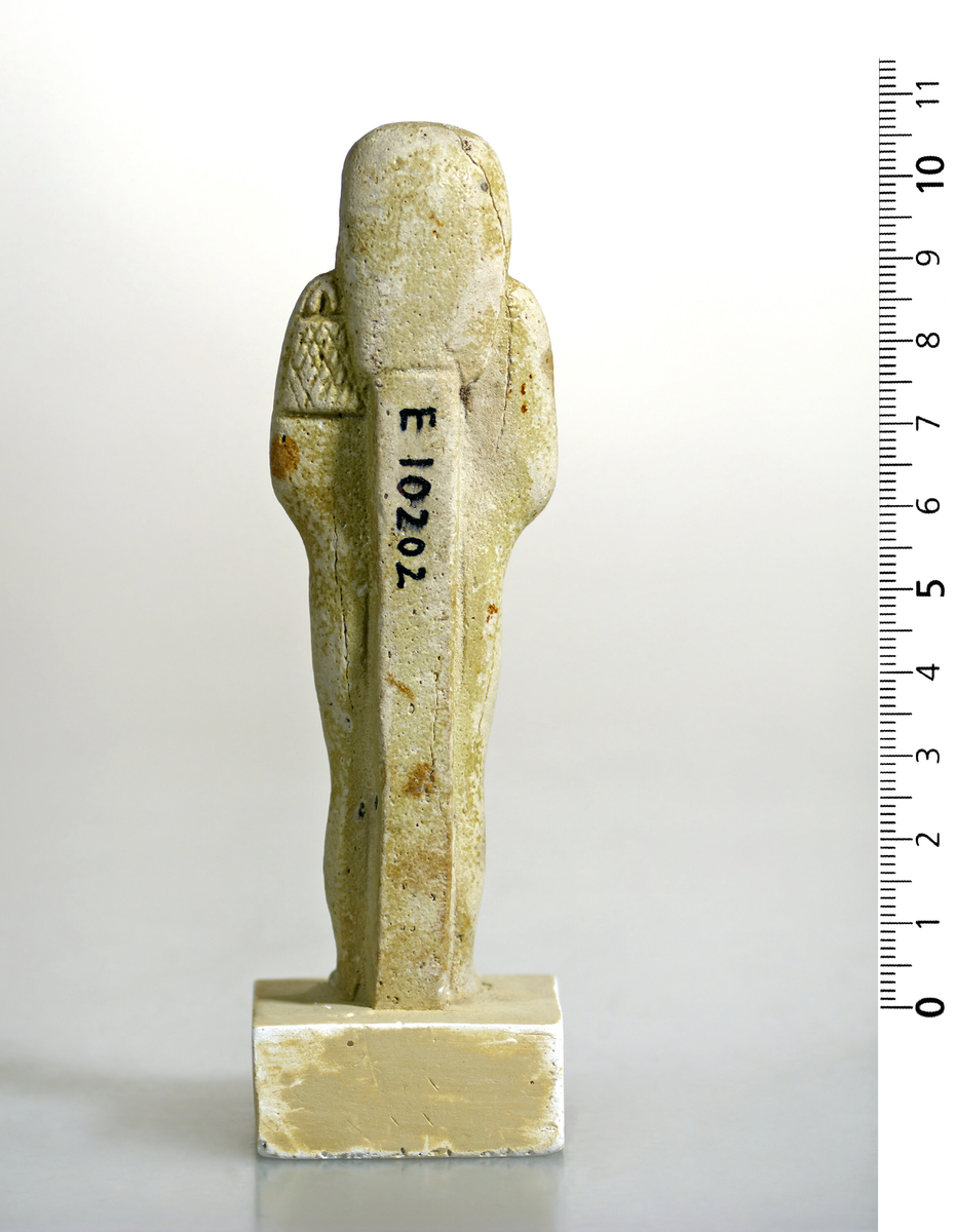 Ushabti i hvit-gul fajanse med tydelige hieroglyfer foran. Pene trekk. 10,5 cm høy.
Fajanse