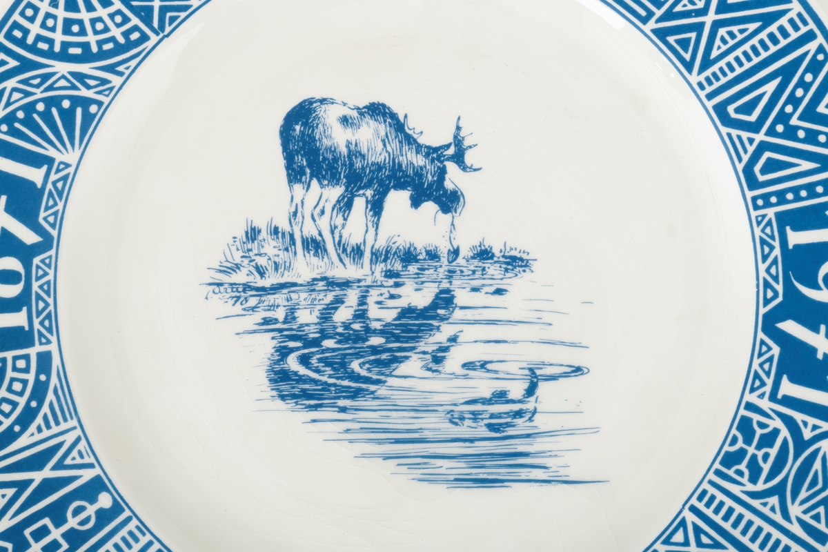 Tallerken, porodusert i forbindelse med Norges Jeger- og Fiskerforenings 100-årsjubileum i 1971. Det er en rund tallerken med 28,4 centimeters diameter. Den sentrale delen er forholdsvis plan, men med oppoverbuete sidekanter som danner ei skål med snaut 20 centimeters diameter. Utenfor dette partiet er det en 4,3 centimeter bred utoverskrånende kant. Tallerkenen er kvit, men har blå dekor. Sentralt i skåla har man gjengitt ei strektegning av en elg som slurper i seg vann og vannplanter i strandsona mot et skogstjern, der den speiles i vannflata. I vannet, og noe mindre framtredende, skimter vi en fisk som har skapt ringer på vannspeilet. Rundt ytterkanten av tallerkenen er det en slags bord som er blå med kvite streker. Her finner vi den jubilerende organisasjonens initialer, «N.J.F.F.», der de to første og de to siste bokstavene skilles av organisasjonens logo, et stilisert reinhode med gevir omgitt av en ring med stiliserte fisker. Også årstallene «1871» og «1971» og en påminnelse om den mellomliggende perioden «100 ÅR» som ble feiret med jubileum inngår i kantdekoren. På undersida av tallerkenen er det en sirkeformet vulst med ytre diameter på 15 centimeter som skulle sikre at tallerkenen sto støtt på et plant underlag. I denne vulsten er det to gjennombrutte hull for eventuell opphengshempe. Sentralt på undersida finner vi produsentens logo - ei stilisert steinøks med produsentens navn «STAVANGERFLINT» i en hesteskoform rundt skaftet. Under finner vi opphavslandet «NORWAY» på ei rett linje.

Dette er en tallerken som det naturligvis gikk an å spise middagsmat fra, eller kanskje til å servere småkaker på, men det var nok neppe med tanke på slike funksjoner den ble produsert. Tallerkenen var nok primært et utstillingsobjekt som skulle markere tilhøringhet til organisasjonen Norges Jeger- og Fiskerforbund og delaktighet i dens jubileumsfeiring. Hva man feiret framgår av en historisk artikkel som er gjengitt under fanen «Opplysninger».