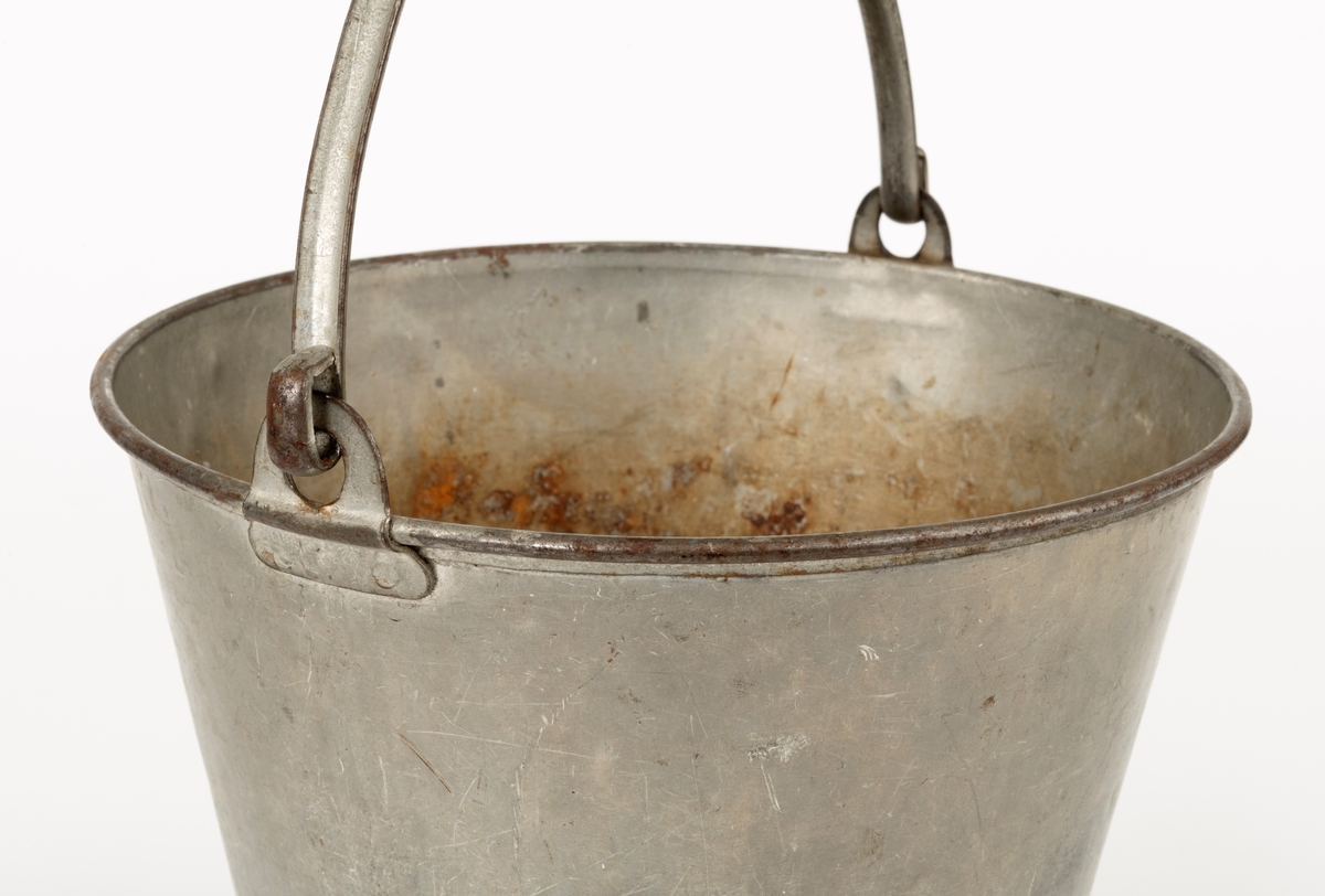 Bøtte av den typen det var vanlig å bære vann i. Bøtta er sveiset ihop av jernblikk. Den er rund, med en diameter som øker fra standflata (18,4 centimeter) til overkanten (27,1 centimeter). Høyden på sjølve beholderen er 23,4 centimeter, regnet fra underlaget til overkanten. I den nedre enden er det en forsterkende fals. Botnplata er noe nedoverbuket. Ved overkanten, diametralt plassert i forhold til hverandre, er det påsveiset «ører» med gjennombrutte hull for feste av bærehanken, som er buet i halvsirkelform. Den ene av disse er plassert over sveiseskjøten som binder plata i sideveggen sammen, og har dermed fungert som forsterkende element i tillegg til å være hankfeste. Hanken er lagd av 2,35 millimeter tjukt galvanisert jern. Den er 1,14 centimeter bred og har et U-formet tverrsnitt, der den runde sida er nedovervendt, slik at hanken ikke skulle gnage i fingrene på bæreren. Bøtta har noe rust i den innvendige botnen, men den er fortsatt tett. Den rommer drøyt 8 liter væske når den fylles breddfull.