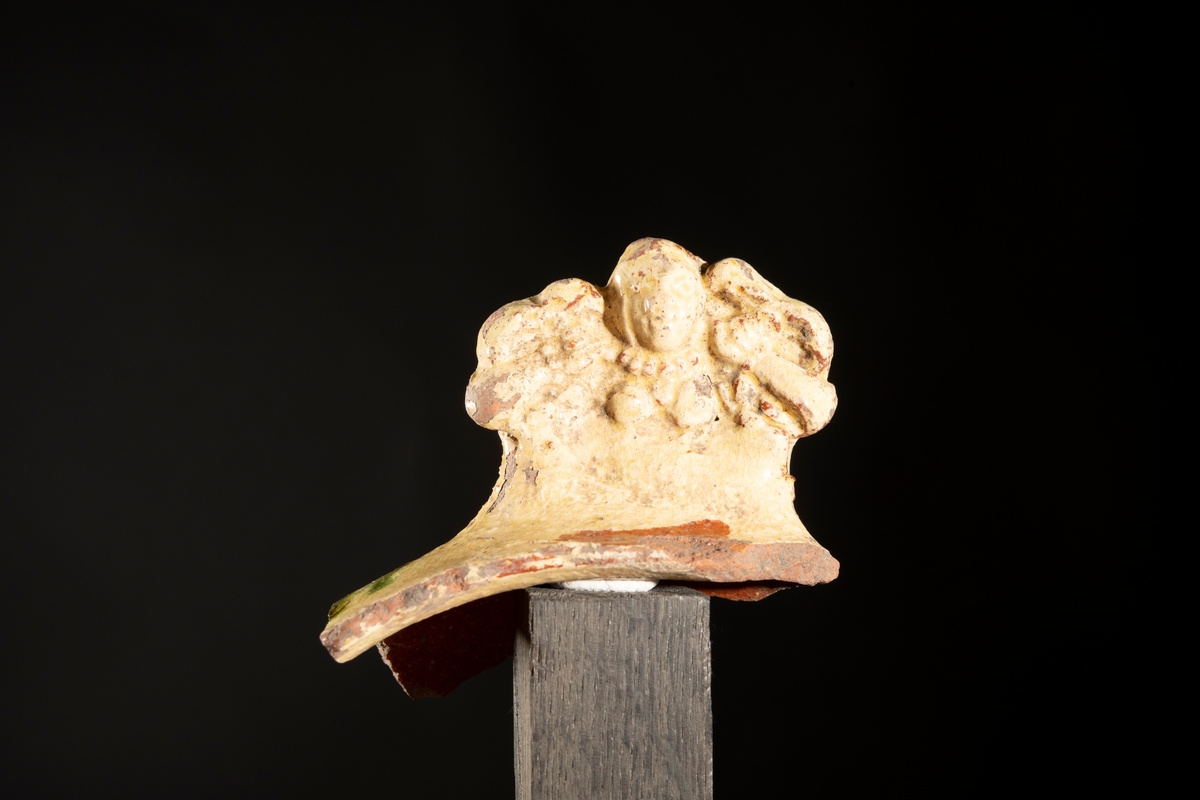 Motivet med den tvestjärtade sjörjungfrun, även kallad melusine, är pressat in i leran med en stämpel. Handtagets ytterform följer sjöjungfruns former som är symetriska med de två fiskstjärtarna mot fästet mot skålen och jungfruns huvud mot ytterkanten av handtaget. Stilen är holländsk barock och de flesta fynd med denna dekor är daterade till 1660-tal.