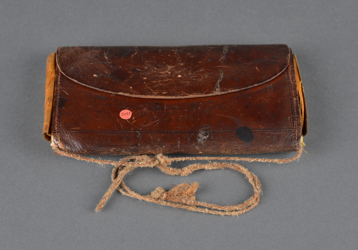 Seddelbok i lær og papir.
Er utbrettbar med en klaff foran. Romdelere i lommeboka er laget av papp/papir. Inneholder ei notisbok hvor det er listet opp varer med priser. Usikkert om det er handlelister eller om dette ble brukt med kreditt på butikken. 
Har en liten hempe på baksiden, kanskje for å henge i belte eller lignende