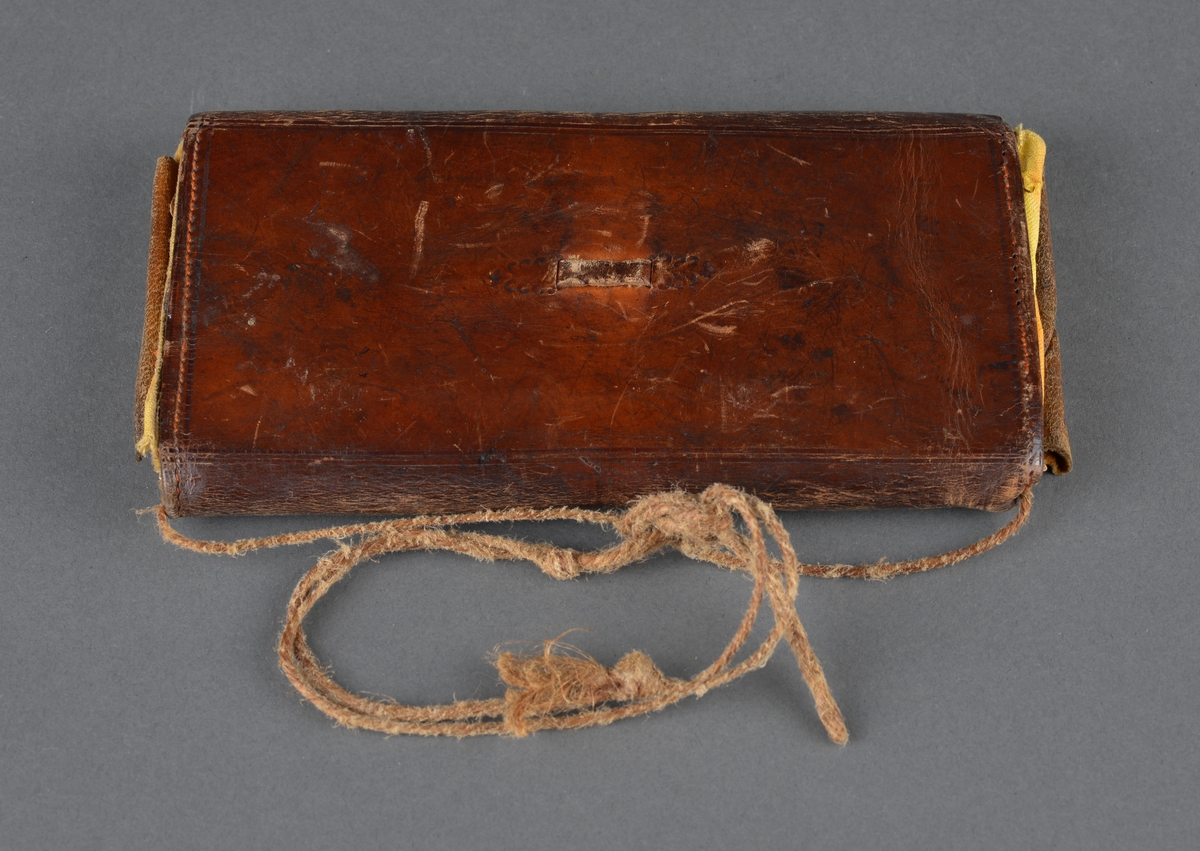 Seddelbok i lær og papir.
Er utbrettbar med en klaff foran. Romdelere i lommeboka er laget av papp/papir. Inneholder ei notisbok hvor det er listet opp varer med priser. Usikkert om det er handlelister eller om dette ble brukt med kreditt på butikken. 
Har en liten hempe på baksiden, kanskje for å henge i belte eller lignende