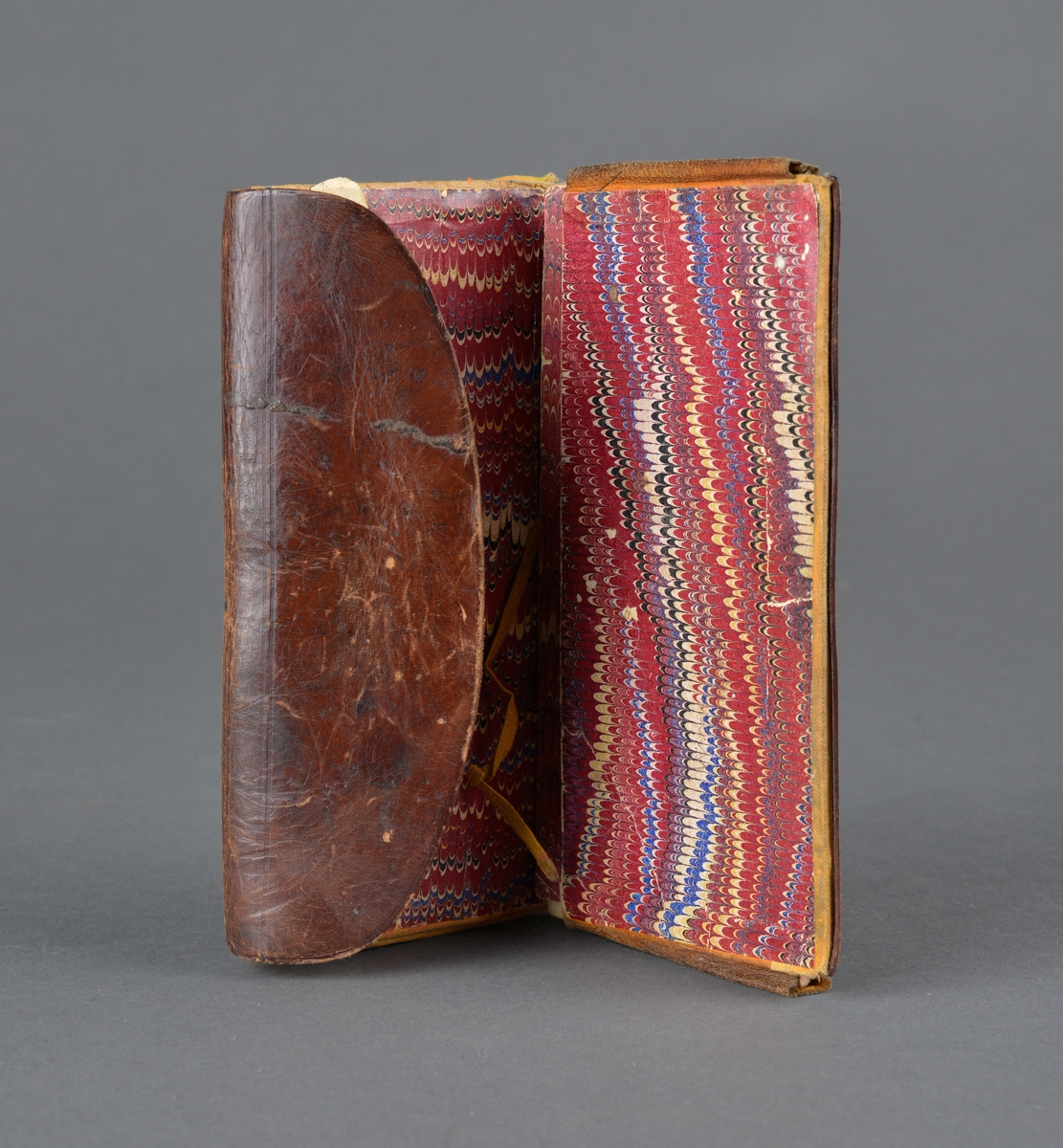 Seddelbok i lær og papir.
Er utbrettbar med en klaff foran. Romdelere i lommeboka er laget av papp/papir. Inneholder ei notisbok hvor det er listet opp varer med priser. Usikkert om det er handlelister eller om dette ble brukt med kreditt på butikken. 
Har en liten hempe på baksiden, kanskje for å henge i belte eller lignende