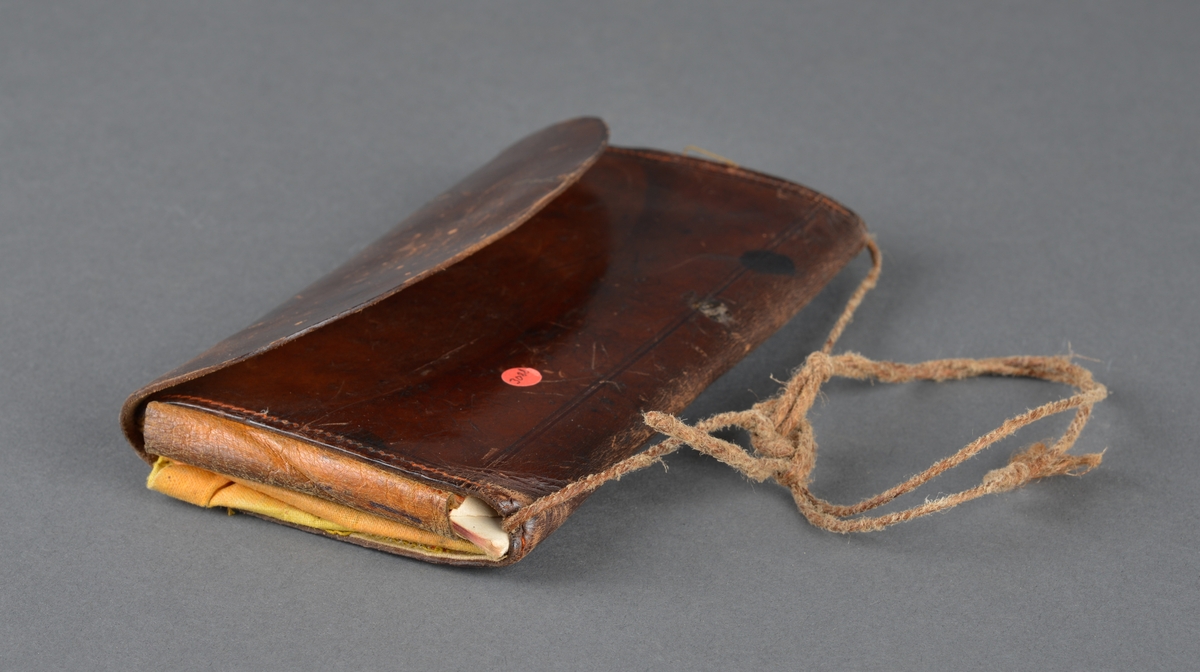 Seddelbok i lær og papir.
Er utbrettbar med en klaff foran. Romdelere i lommeboka er laget av papp/papir. Inneholder ei notisbok hvor det er listet opp varer med priser. Usikkert om det er handlelister eller om dette ble brukt med kreditt på butikken. 
Har en liten hempe på baksiden, kanskje for å henge i belte eller lignende