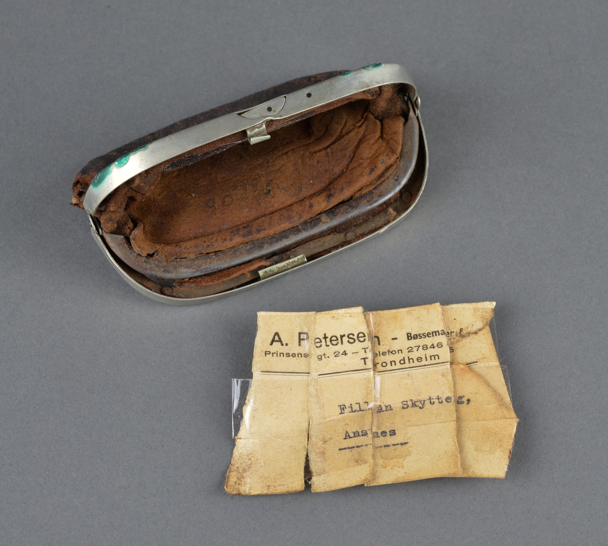 Pengepung i lær og metall
Beslag med lås og invendige romdelere er laget i metall (antatt messing). 
Pengepungen har tilhørt Alfred Risvik (Petters far) 
Inni pengepunger lå papirlapper, som er limt sammen til en adresselapp fra A.Petersen Bøssemaker til Fillan Skytterlag, Ansnes. Alfred var med i skytterlaget på Ansnes.