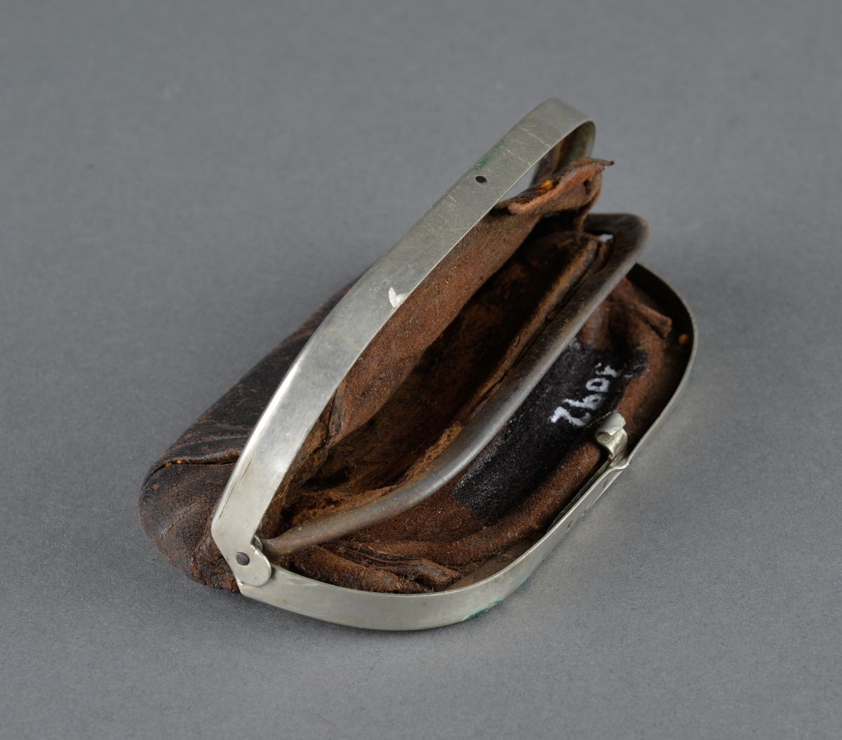 Pengepung i lær og metall
Beslag med lås og invendige romdelere er laget i metall (antatt messing). 
Pengepungen har tilhørt Alfred Risvik (Petters far) 
Inni pengepunger lå papirlapper, som er limt sammen til en adresselapp fra A.Petersen Bøssemaker til Fillan Skytterlag, Ansnes. Alfred var med i skytterlaget på Ansnes.