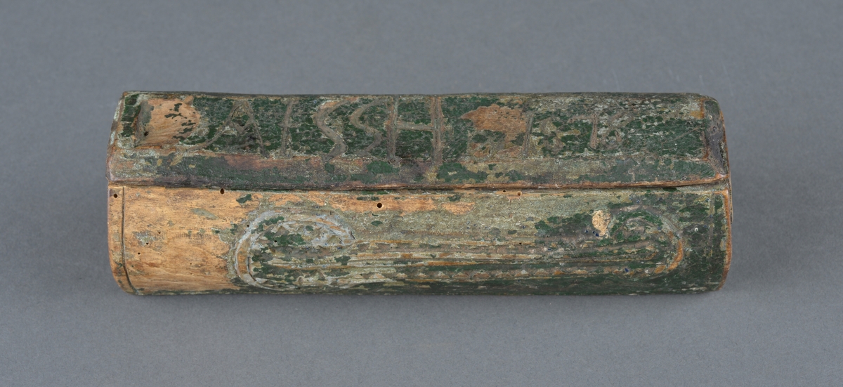 Trepenal for oppbevaring av nåler og annet. 
Er fremstilt av uthulet trevirkeog har et lokk som skyves på plass. 
Inne i penalet ligger ei nål. 

Dekor langs penalets sider. Ulike former med trekantmønster.

Flere inskripsjoner på penalet og lokket. På sidene er det risset inn et kors med endestykker og tre langsgående linjer under nederste eller øverste del av korset. Ukjent hva dette kan bety, om det har ei mening eller bare er til dekor.