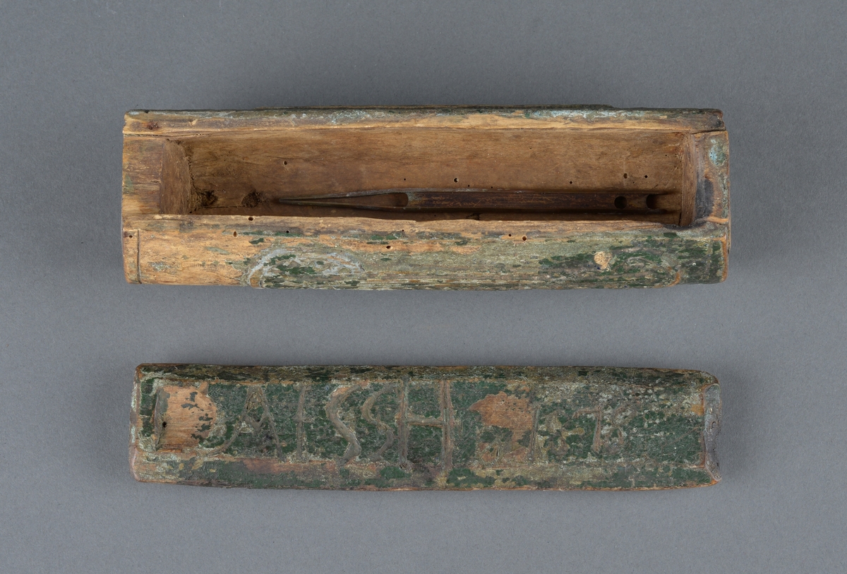 Trepenal for oppbevaring av nåler og annet. 
Er fremstilt av uthulet trevirkeog har et lokk som skyves på plass. 
Inne i penalet ligger ei nål. 

Dekor langs penalets sider. Ulike former med trekantmønster.

Flere inskripsjoner på penalet og lokket. På sidene er det risset inn et kors med endestykker og tre langsgående linjer under nederste eller øverste del av korset. Ukjent hva dette kan bety, om det har ei mening eller bare er til dekor.