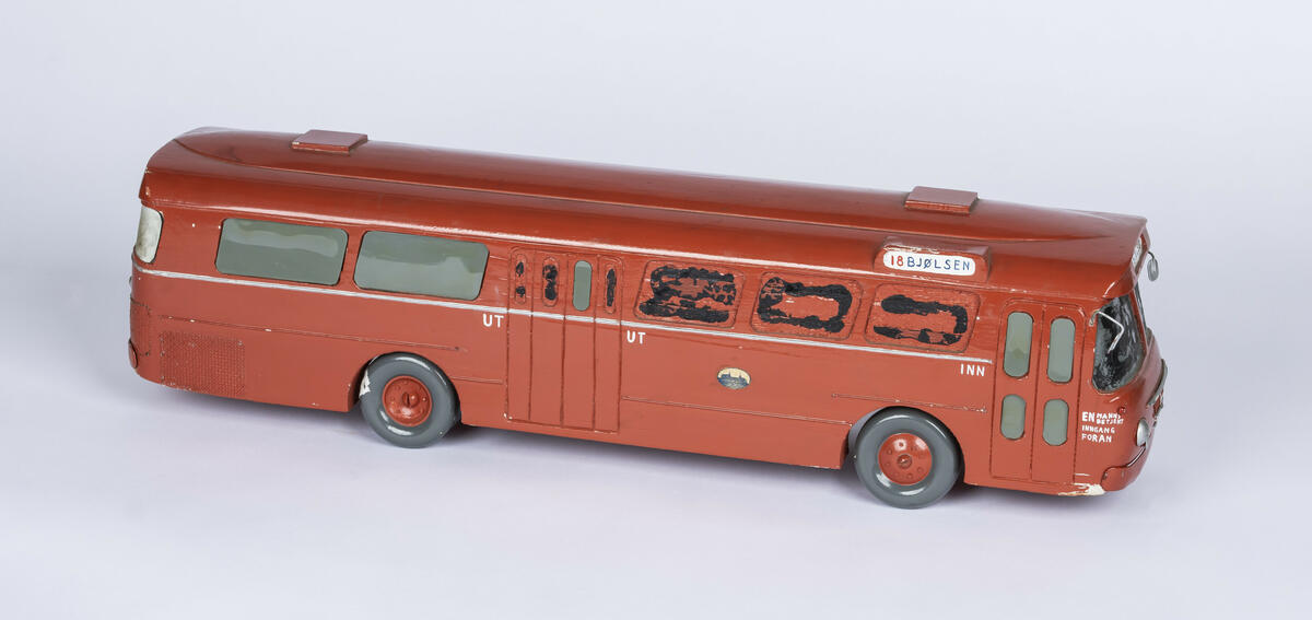 Tremodell av Oslo Sporveiers buss A-15730. Modellen er malt rød, med en hvit stripe langs siden. Bussen har detaljerte utskjæringer for dører og vinduer, og detaljer på taket. 