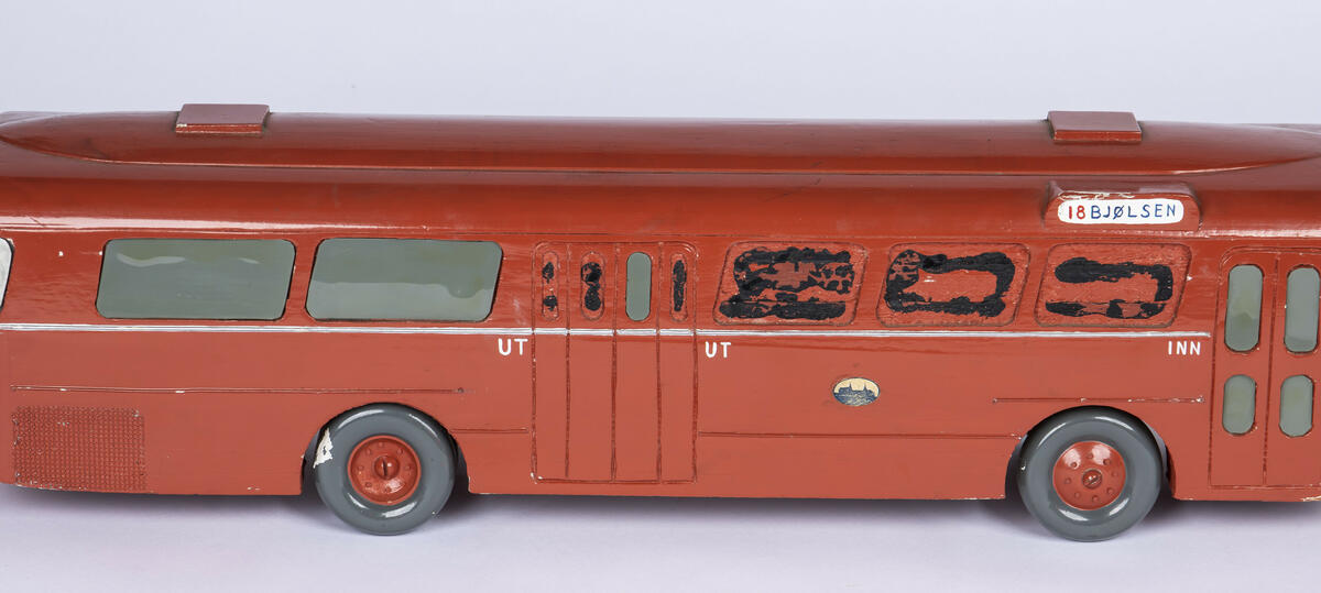 Tremodell av Oslo Sporveiers buss A-15730. Modellen er malt rød, med en hvit stripe langs siden. Bussen har detaljerte utskjæringer for dører og vinduer, og detaljer på taket. 