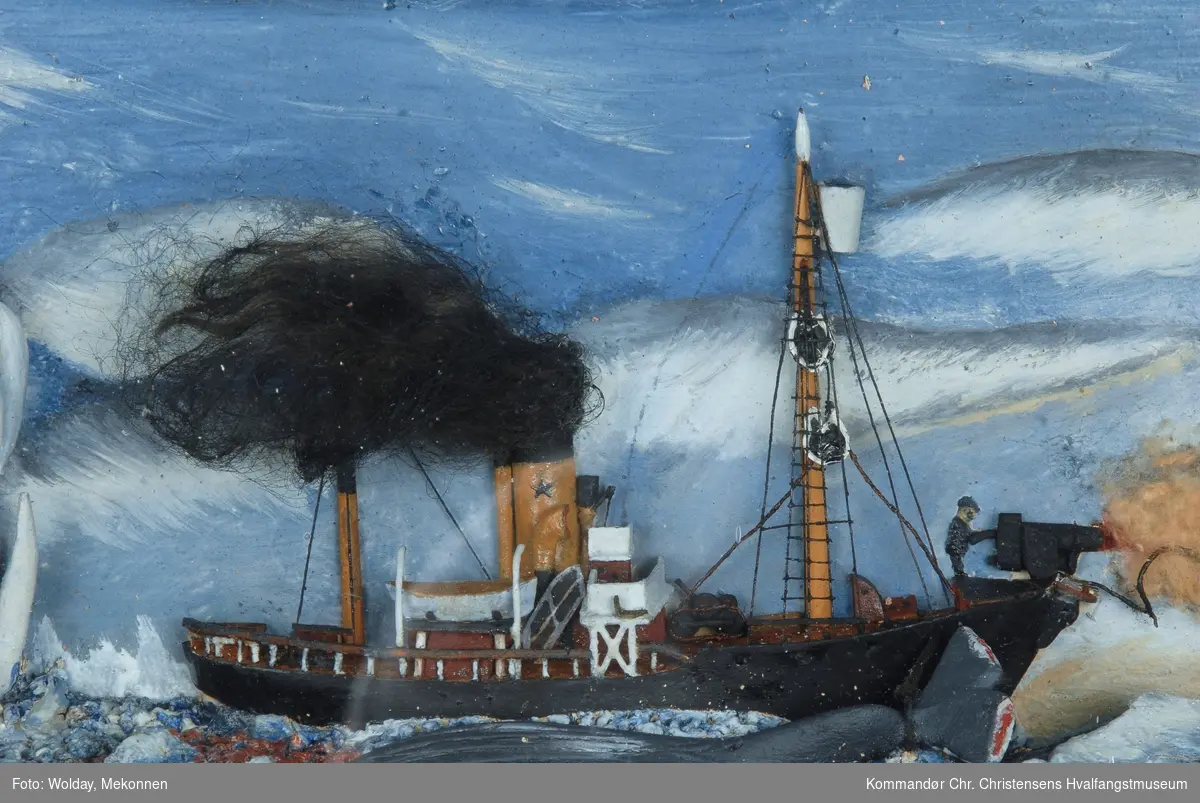 Fangstscene: Hvalbåten "Falk" i halvmodell i Sydishavet, en stjerne i skorstenen. Hvalskytter fanger hval m/harpun. En hval er fanget og ligger langs båtsiden.