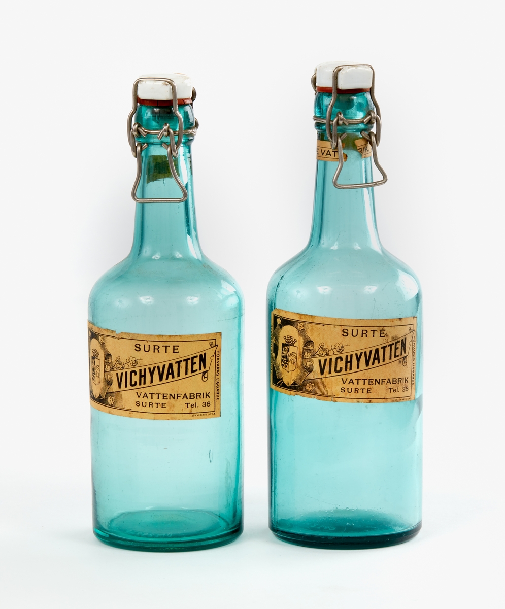 Två flaskor av gröntonat klarglas. Etikett med text, bla: "Vichyvatten". Surte vattenfabrik. Knäppkapsyl av poslin och metallbygel samt gummiring.