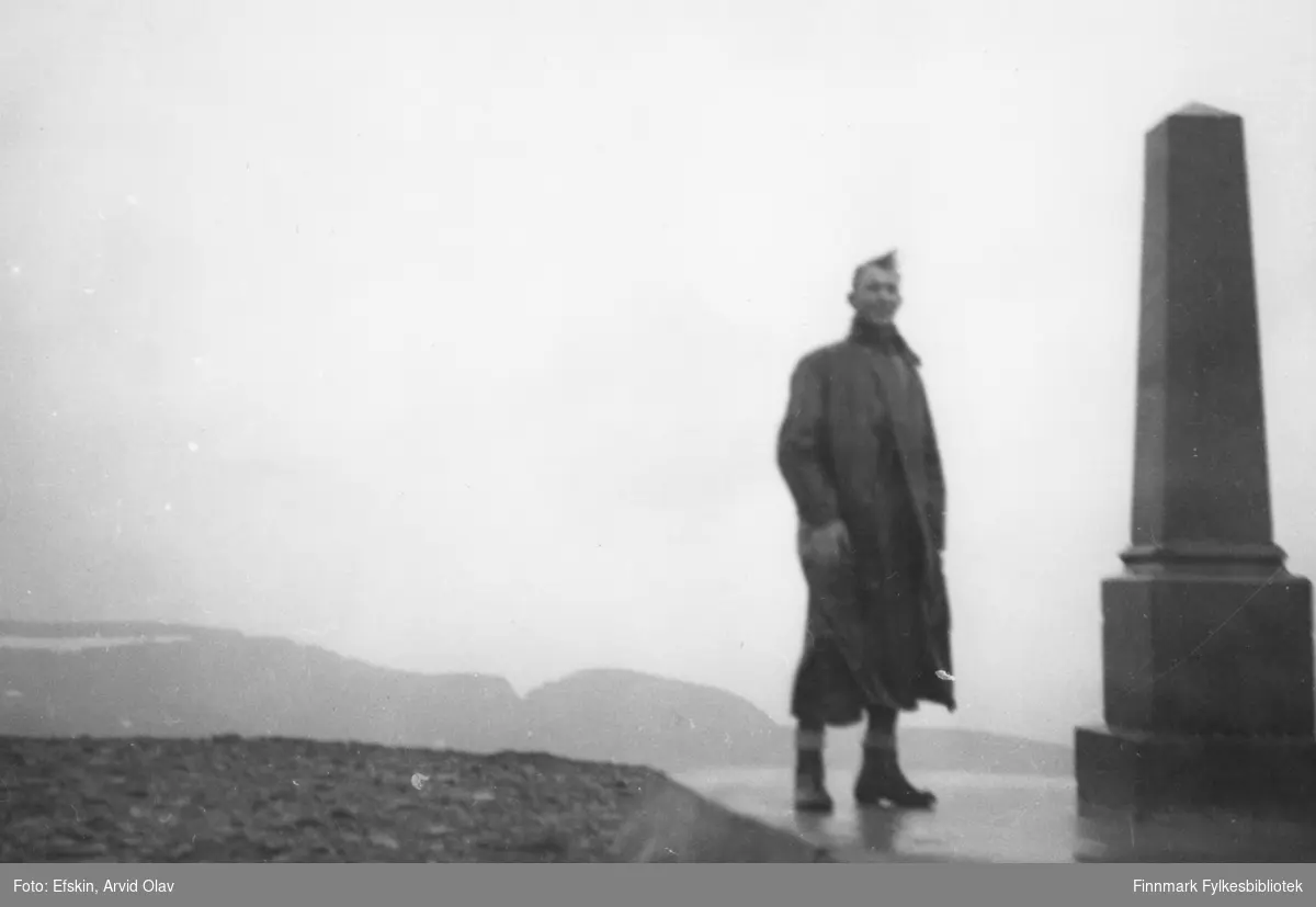 En mann står ved siden av "Oscarstøtten" på platået i Nordkapp, 1939. Den ble avduket av kong Oscar II den 2. juli 1873.