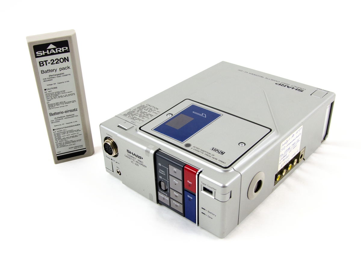 Videobandspelare VC-220, tillverkad av Sharp Electronics Corporation i Tochigi, Japan, november 1982. Rektangulärt föremål i grå plast med uttag för att koppla in kamera, mikrofon för inspelning samt skärm och högtalare för uppspelning. Maskinen är utrustad med batteri för att fungera utan kabel och använder kompakt VHS-kassettformat, VHSC. På föremålets sida finns en handskriven anteckning "Inköpt för AJ 37 CCD-kamerastudie hos SAAB 1984-85 Sharp VC-220 nr 911331 NTSC VHS-C".