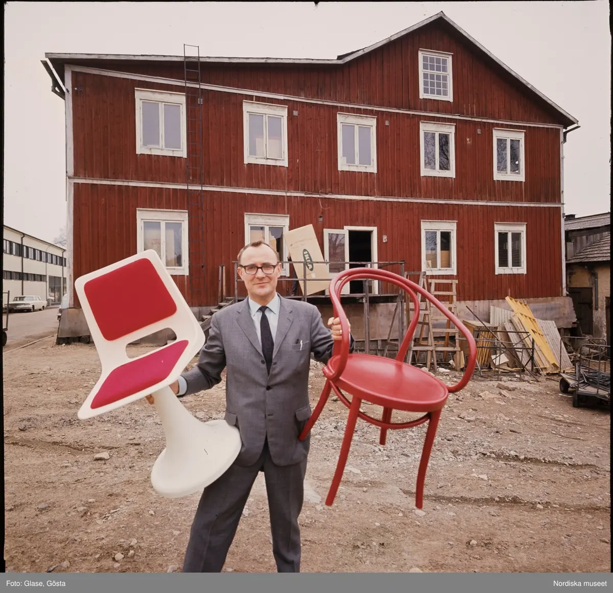 IKEA-grundaren Ingvar Kamprad med ett par stolar i händerna, framför ett rött hus.