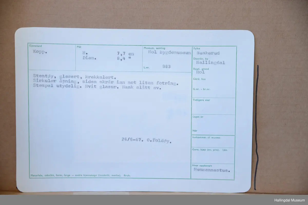 Sirkulær åpning, siden skrår inn mot liten fotring. Stempel utydelig. Hvit glasur. Hank slått av.
26/6-67. O. Foldøy.