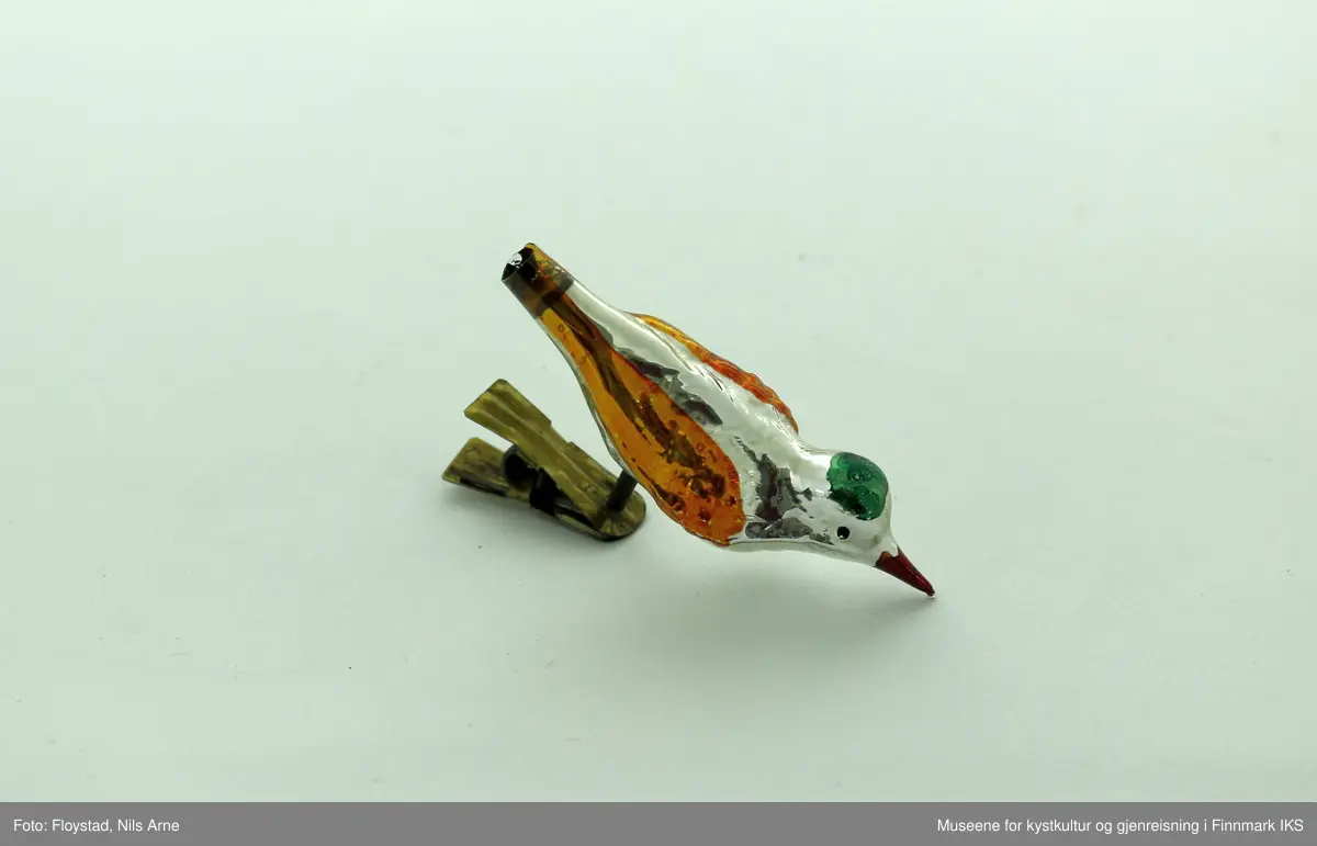 To små juletrefugler laget av plast og med metallfeste. Fuglene har en blank aluminiumsfarge, med påmalte farger. Vinngene er gullfargede, nebbet er rødt og på toppen av hodet er det påmalt en grønn sirkel.