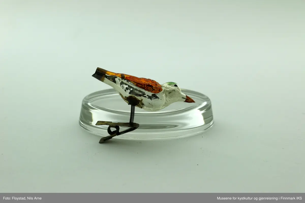 To små juletrefugler laget av plast og med metallfeste. Fuglene har en blank aluminiumsfarge, med påmalte farger. Vinngene er gullfargede, nebbet er rødt og på toppen av hodet er det påmalt en grønn sirkel.