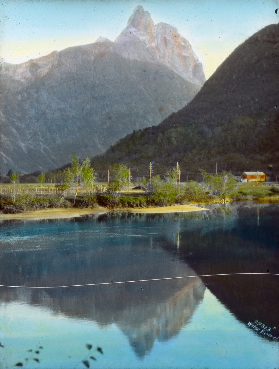 Håndkolorert dias. Utsikt mot Romsdalshorn. I forgrunnen sees Sogge bro og en rødmalt låve.