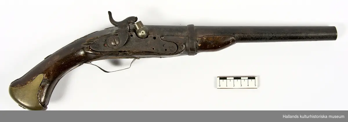 Slaglåspistol försedd med halvstock. Kolv och stock i trä (ek). Kolvbeslag av mässing och mekanik i järn. Varbygel och beslag på pistolens vänstra sida av mässing har tillkommit efter jordfynd. Framstocken saknar laddstocksränna. Pipan har en innerdiameter  på c:a 16mm och i piprännan sitter en kula av senare datum fastkilad; troligtvis en spelkula.