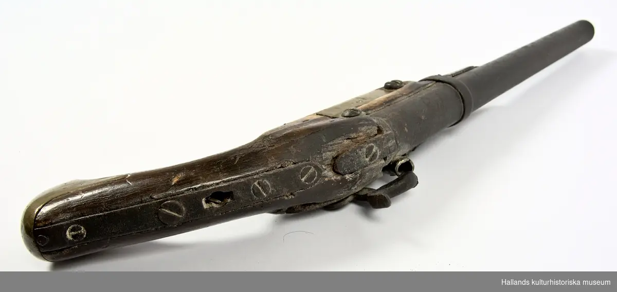 Slaglåspistol försedd med halvstock. Kolv och stock i trä (ek). Kolvbeslag av mässing och mekanik i järn. Varbygel och beslag på pistolens vänstra sida av mässing har tillkommit efter jordfynd. Framstocken saknar laddstocksränna. Pipan har en innerdiameter  på c:a 16mm och i piprännan sitter en kula av senare datum fastkilad; troligtvis en spelkula.