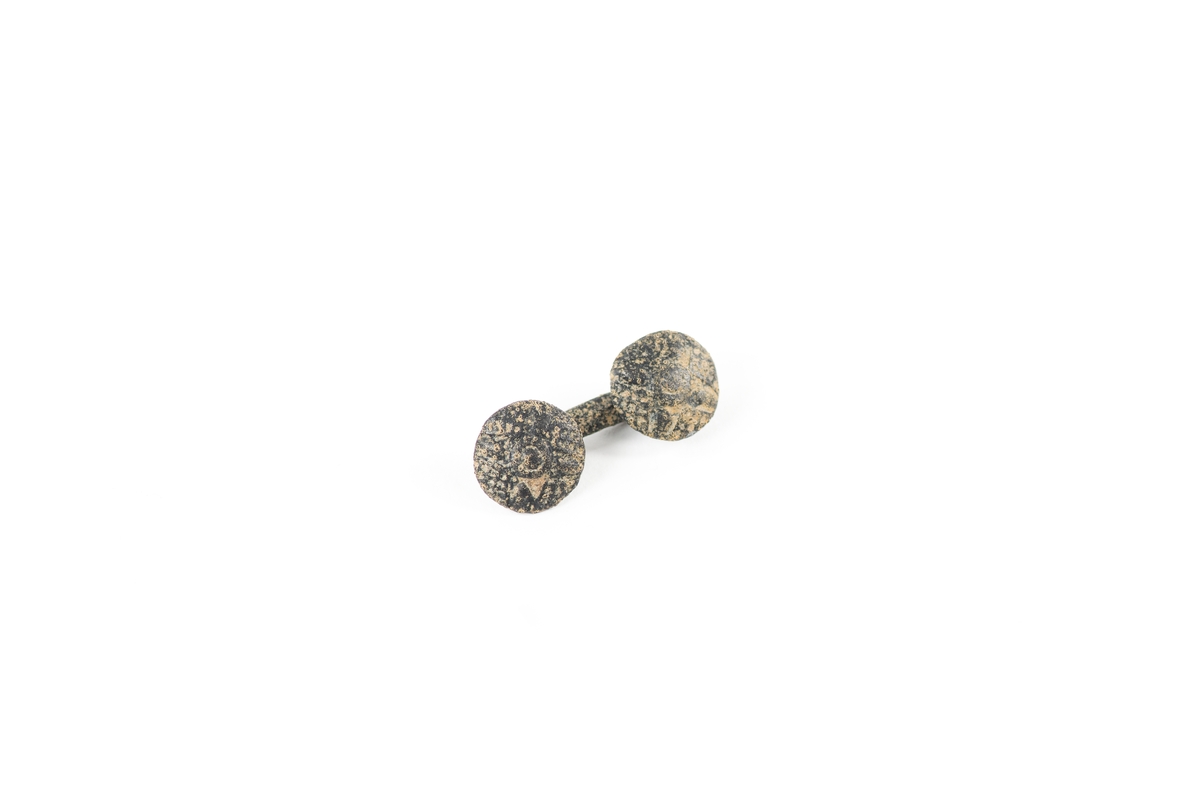 Manschettknapp möjligen av silver. Knapp bestående av en stång med två runda knappar i båda ändar. Knappar är dekorerade med geometriska mönster.