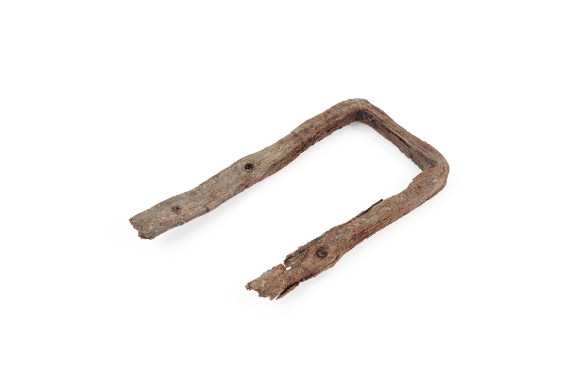 Järnbeslag, u-formad profil, gjort av järn. Tillverkad av fyrkantig järnstång som mäter 2,3 x 2,1 cm. Ändarna tillplattade till 3,4 x 1 cm, med två spikar/hål, men brutna i änden.
