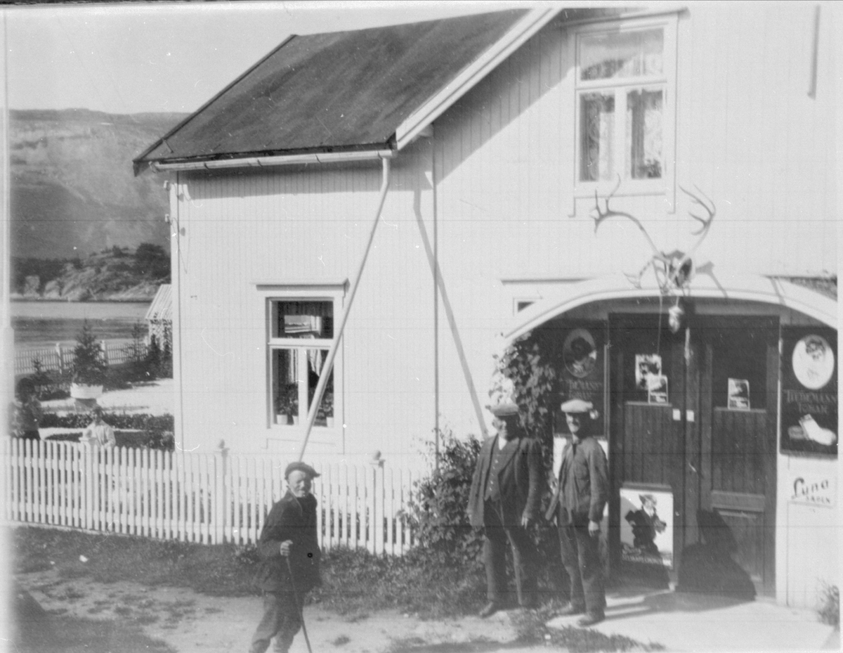 Amatørportrett av tre menn utenfor det gamle inngangspartiet på butikken S. A. Tandes Eftf. i Grov.