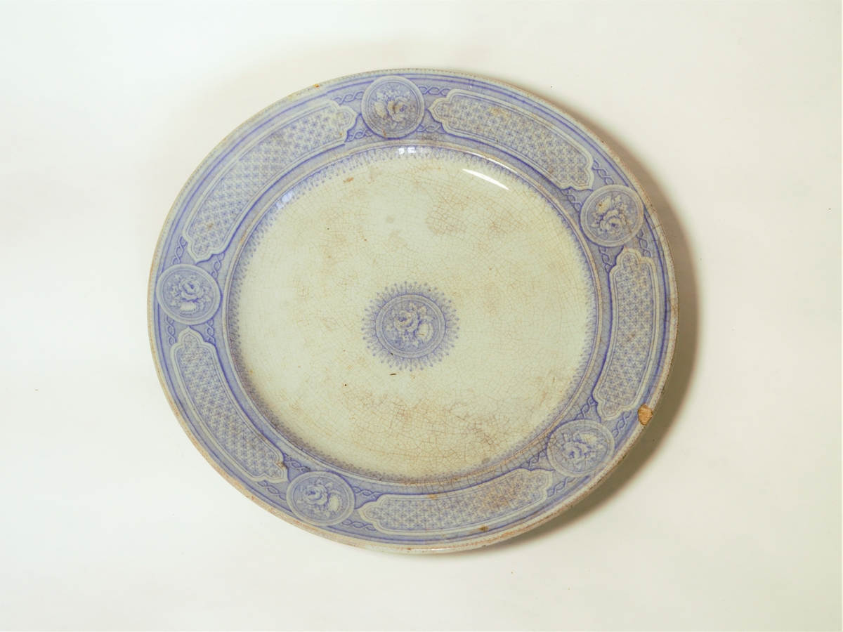 4 stk. tallerkener. Sirkulært snitt, med påtrykket dekor i lilla.
Klassiske border langs ytterkantene.
Dekorteknikk: Trykket.
Motiv: Klassisk bord langs ytterkant og rose i midten.

Se også varmefat: FFB 549