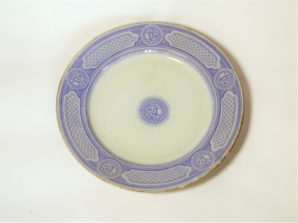 4 stk. tallerkener. Sirkulært snitt, med påtrykket dekor i lilla.
Klassiske border langs ytterkantene.
Dekorteknikk: Trykket.
Motiv: Klassisk bord langs ytterkant og rose i midten.

Se også varmefat: FFB 549