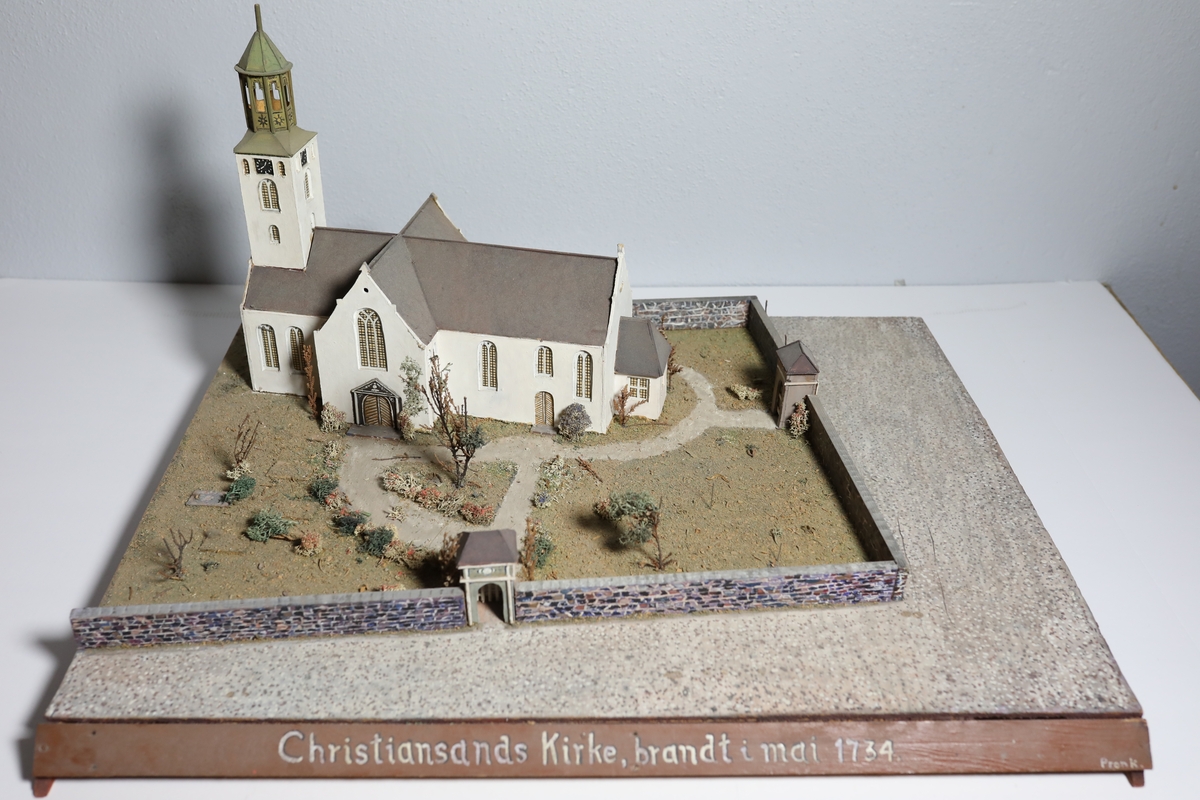 Stor rektangulær modell av Kristiansands andre domkirke. Den har mange likheter med Appel sitt maleri av domkirken fra 1827, som kan tyde på at det var hans hovedkilde. Deler av muren og torget rundt er del av modellen. Det er brukt mose og kvister for å dekorere kirkegården.