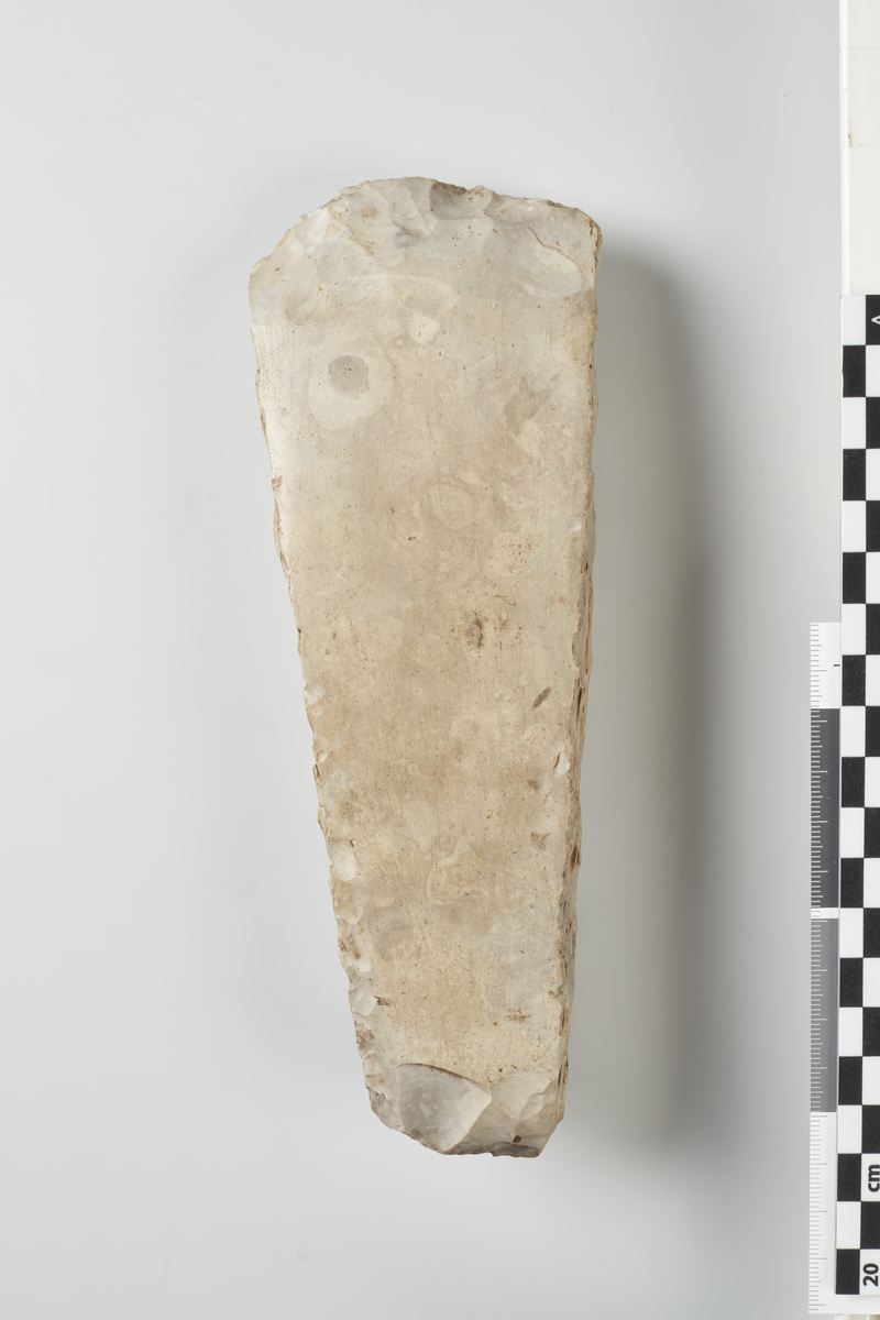 Flintøxe (eller Meisel), sandsynlig oprindelig af samme Form, men Banepartiet mangler. Er nu 20 cm. lang, altsaa oprindelig af betydelig Størrelse. (12220).