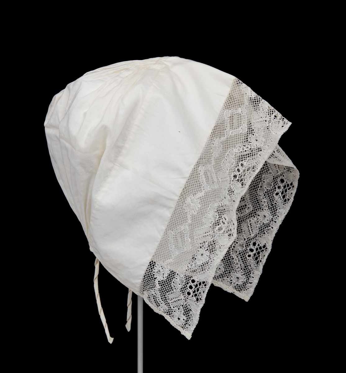 Hatt till Malungs sockendräkt för kvinna. Av vitt tunnt bomullstyg. 85 mm bred fåll framtill. Längs framkanten knypplad spets. Tätt hoprynkat bakparti. På insidan mitt uppe en liten förstärkningslapp, på utsidan litet broderi. Smal fåll nedtill. Två smala knytband.