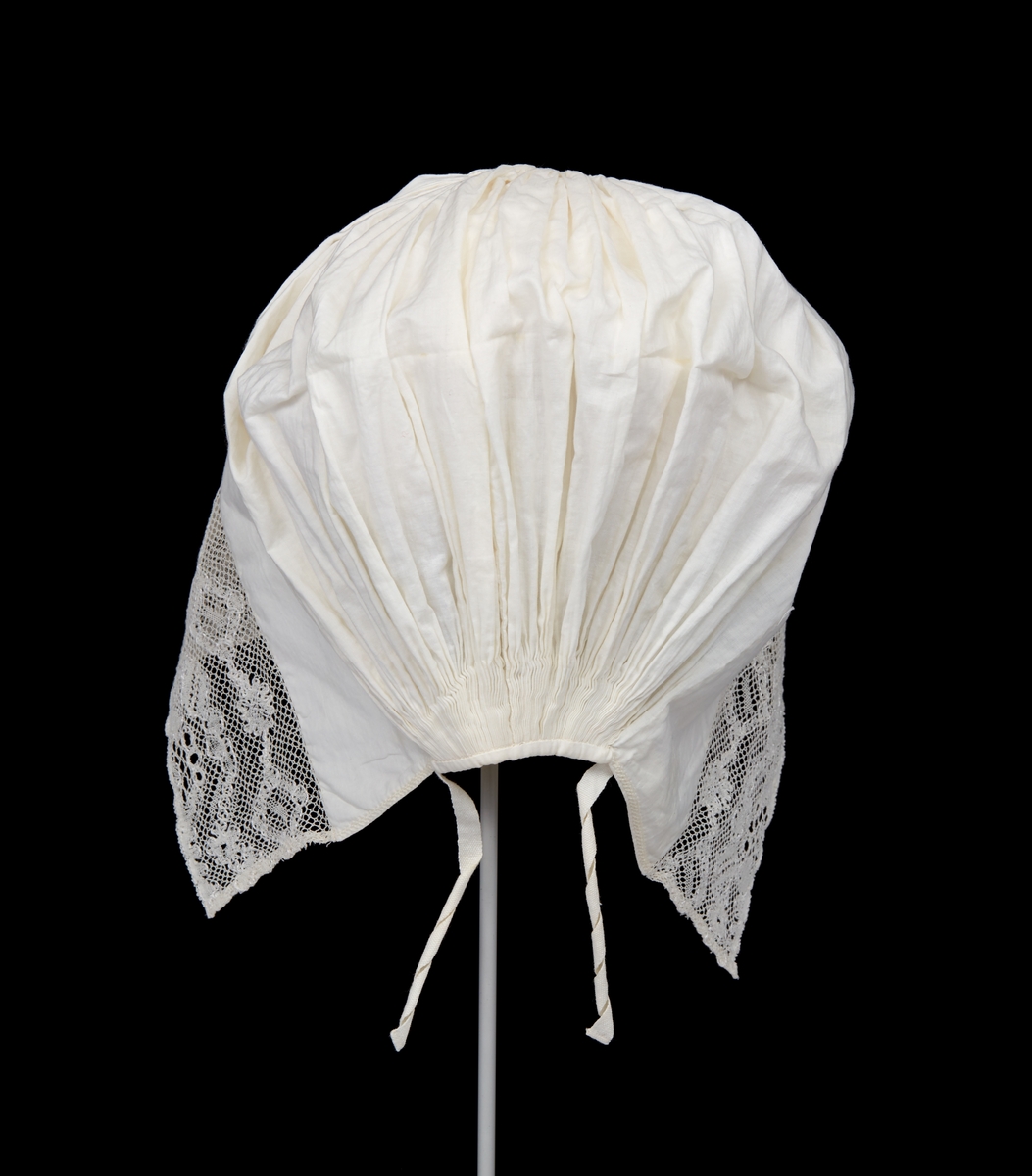 Hatt till Malungs sockendräkt för kvinna. Av vitt tunnt bomullstyg. 85 mm bred fåll framtill. Längs framkanten knypplad spets. Tätt hoprynkat bakparti. På insidan mitt uppe en liten förstärkningslapp, på utsidan litet broderi. Smal fåll nedtill. Två smala knytband.