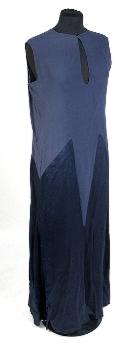 Rak aftonklänning i blått atlassiden. Ihopsydd av snedskurna kilformade våder, omväxlande på rät- och avigsida. 2 st. kilformade våder fram till midjehöjd. Pålagt stycke (med avigsidan ut) med kil 43 cm från midjan och ned. Den påsydda tygdelen är svängd och avslutad i spetsform 13 cm från halsringningen mitt fram. Bakvåden klippt i 1 stycke med kil 43 cm från midjan och ned. Rund halsringning, lite mindre bak, 0,5 cm bandkantning runt om, knäppes mitt bak med 1 tryckknapp. 20,5 cm långt sprund från halsringningen mitt bak. Ärmlös med 0,5 cm bandkantning i ärmkanten. 0,3 cm fåll nedtill på klänningen som gör kanten vågig. 
Mått i cm: längd 143, axel 1,5, midja 96.