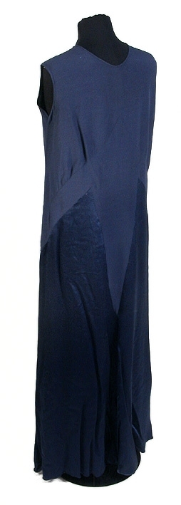 Rak aftonklänning i blått atlassiden. Ihopsydd av snedskurna kilformade våder, omväxlande på rät- och avigsida. 2 st. kilformade våder fram till midjehöjd. Pålagt stycke (med avigsidan ut) med kil 43 cm från midjan och ned. Den påsydda tygdelen är svängd och avslutad i spetsform 13 cm från halsringningen mitt fram. Bakvåden klippt i 1 stycke med kil 43 cm från midjan och ned. Rund halsringning, lite mindre bak, 0,5 cm bandkantning runt om, knäppes mitt bak med 1 tryckknapp. 20,5 cm långt sprund från halsringningen mitt bak. Ärmlös med 0,5 cm bandkantning i ärmkanten. 0,3 cm fåll nedtill på klänningen som gör kanten vågig. 
Mått i cm: längd 143, axel 1,5, midja 96.