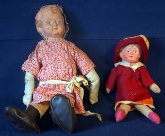 Docka med huvud i papp och kropp i textil stoppad med spån. Blont hår påklistrat upptill på huvudet. Ansikte med målade ögon med ögonbryn och rödmålad mun. Klädd i orange klänning med vit krage, och vinröd blus ovanpå. Mössa (35005:2) i gul textil med tryckta blommor i orange. Mössbrättet i vinrött tyg, samma som blusen.
Dockan är den till höger i bild.