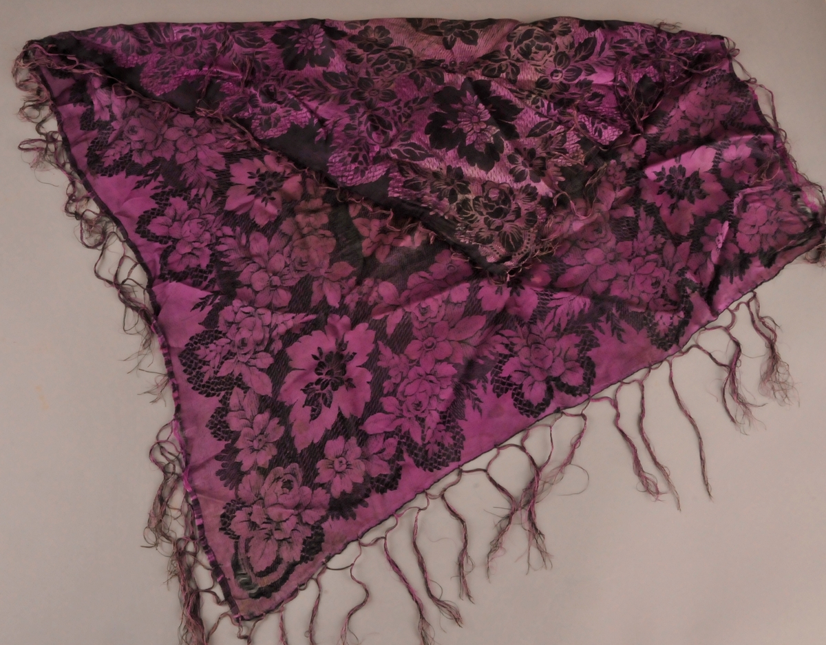 Bringeklut i mønstra silke. Tafs kring alle fire kantane. Ei mørk og ei ljosare side.