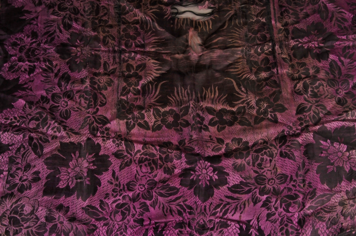 Bringeklut i mønstra silke. Tafs kring alle fire kantane. Ei mørk og ei ljosare side.