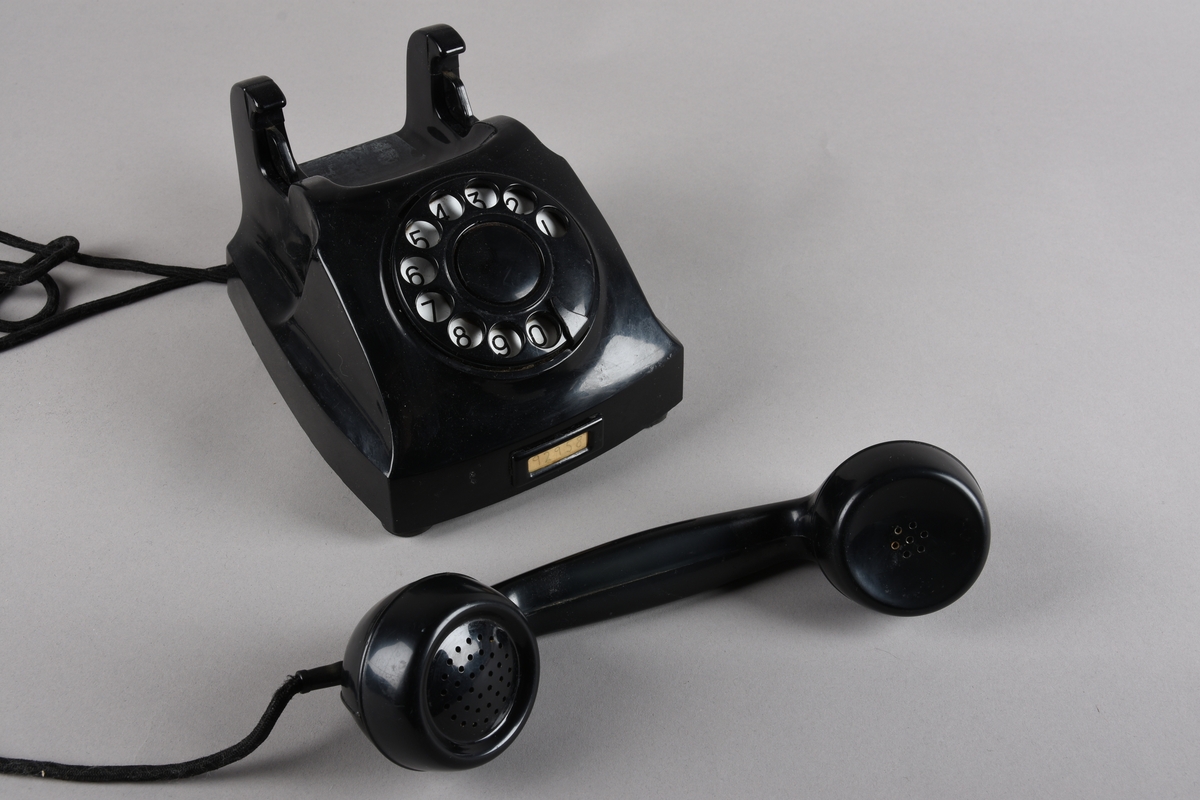 Bordtelefon med telefonrøyr og støpsel for veggkontakt. Apparatet har rektangulær grunnform med skrånande front med talskive frå 0-9. Utanpå talskiva ei skive med 10 hol der ein slår inn kvart tal i telefonnummeret ved å sette fingeren på det talet ein ønsker og dreie skiva mot høgre mot ein stoppar. På toppen av apparatet ein haldar med fjørande brytar, der kontakten vert broten når telefonrøyret ligg på haldaren. Røyret har avlang form med mikrofon i eine enden og høgtalar i andre. Leidning frå røyret til apparatet. Frå apparatet går det leidning med tre-pinna støpsel for telefonkontakt i vegg.