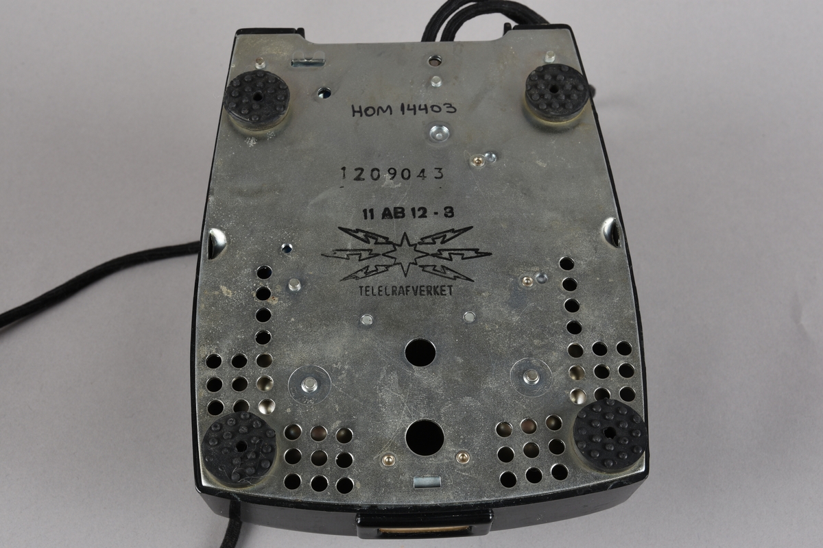 Bordtelefon med telefonrøyr og støpsel for veggkontakt. Apparatet har rektangulær grunnform med skrånande front med talskive frå 0-9. Utanpå talskiva ei skive med 10 hol der ein slår inn kvart tal i telefonnummeret ved å sette fingeren på det talet ein ønsker og dreie skiva mot høgre mot ein stoppar. På toppen av apparatet ein haldar med fjørande brytar, der kontakten vert broten når telefonrøyret ligg på haldaren. Røyret har avlang form med mikrofon i eine enden og høgtalar i andre. Leidning frå røyret til apparatet. Frå apparatet går det leidning med tre-pinna støpsel for telefonkontakt i vegg.
