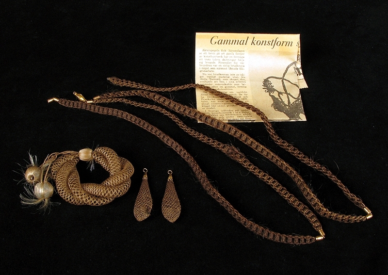 Samling bestående av fyre stycken smycken tillverkade av människohår (hårarbeten).

1: Armband av elastiskt flätat blont hår. Armbandet är försedd med en dekorativ träkula täckt av hår. I kulan har två flätade trådar fästs; trådarna har en hårkula i vardera ände. Diameter: 70 mm

2: Halsband av flätat brunt hår. Halsbandet består av två flätade delar som sammanfogats på längden med ett beslag i gulmetall. Halsbandet har ett lås av gulmetall. Längd: 580 mm

3: Halsband av flätat brunt hår. Halsbandet består av två flätade delar som sammanfogats på längden med ett beslag i gulmetall. Halsbandet har ett lås av gulmetall. Låset är skadat - en del saknas. Se bild. Längd: 580 mm

4 a-b: Örhängen av löst flätat cendrefärgat hår. Droppformade och ihåliga med beslag i gulmetall. Längd: 50mm