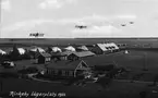 Vykort. Flygbild av Rinkaby lägerplats 1922. Med montage av fyra flygplan i luften.
