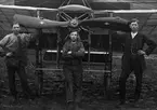 Grupporträtt av personal vid Thulins flygskola på  Ljungbyhed, omkring 1910-1918. Tre unga män står vid flygplan Thulin A framför en hangar.